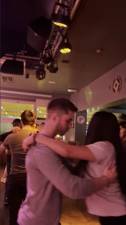 A couple in close bachata hold on a busy social dance floor